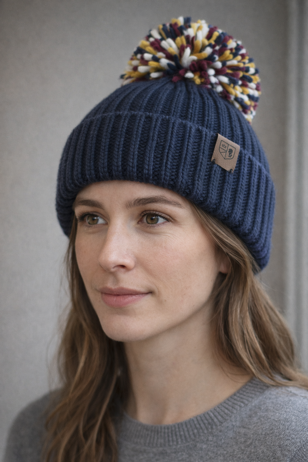Woman wearing a blue knit beanie with a colorful pom-pom against a neutral background