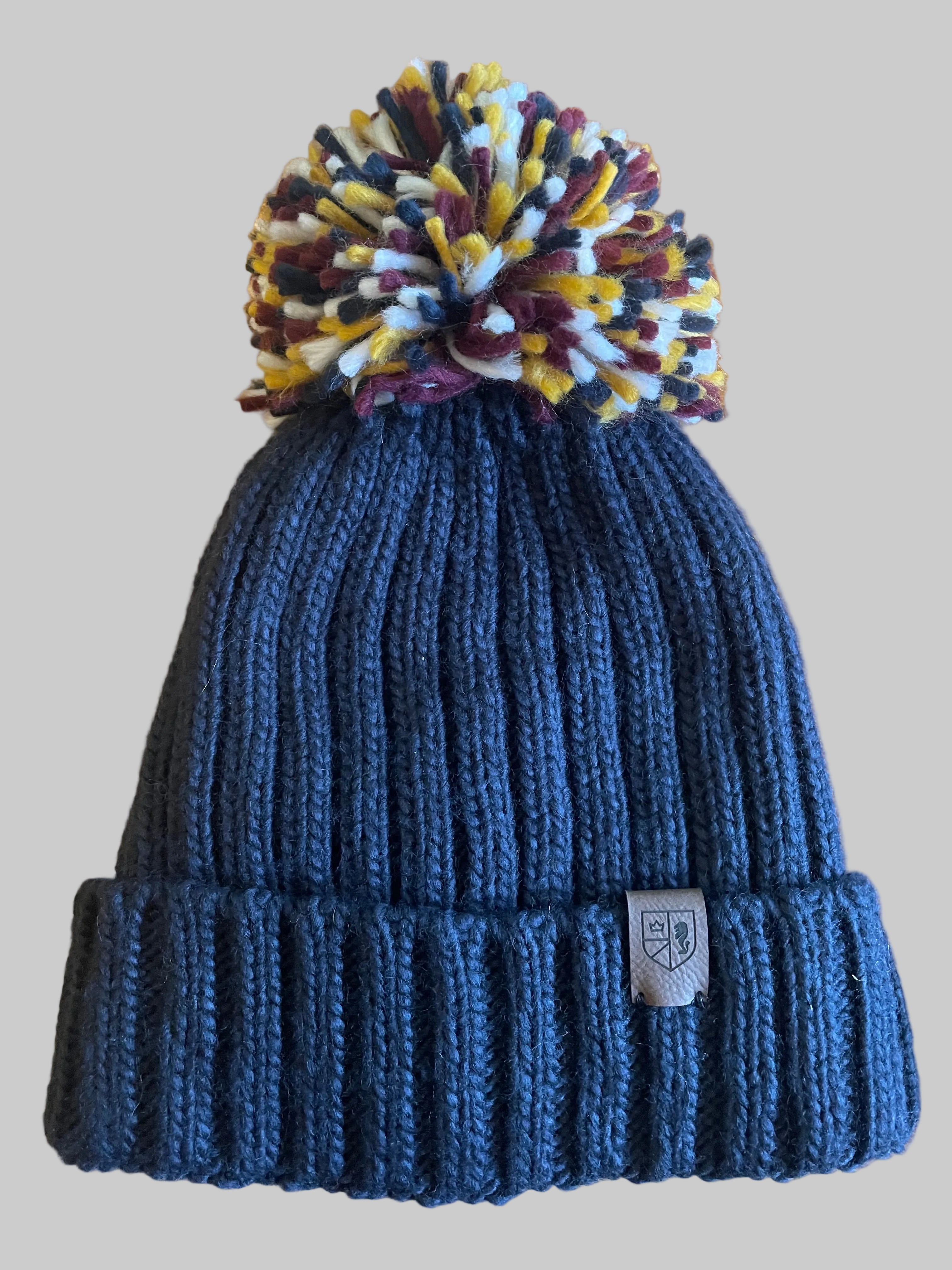 Blue knit beanie with a colorful pom-pom on a wooden surface