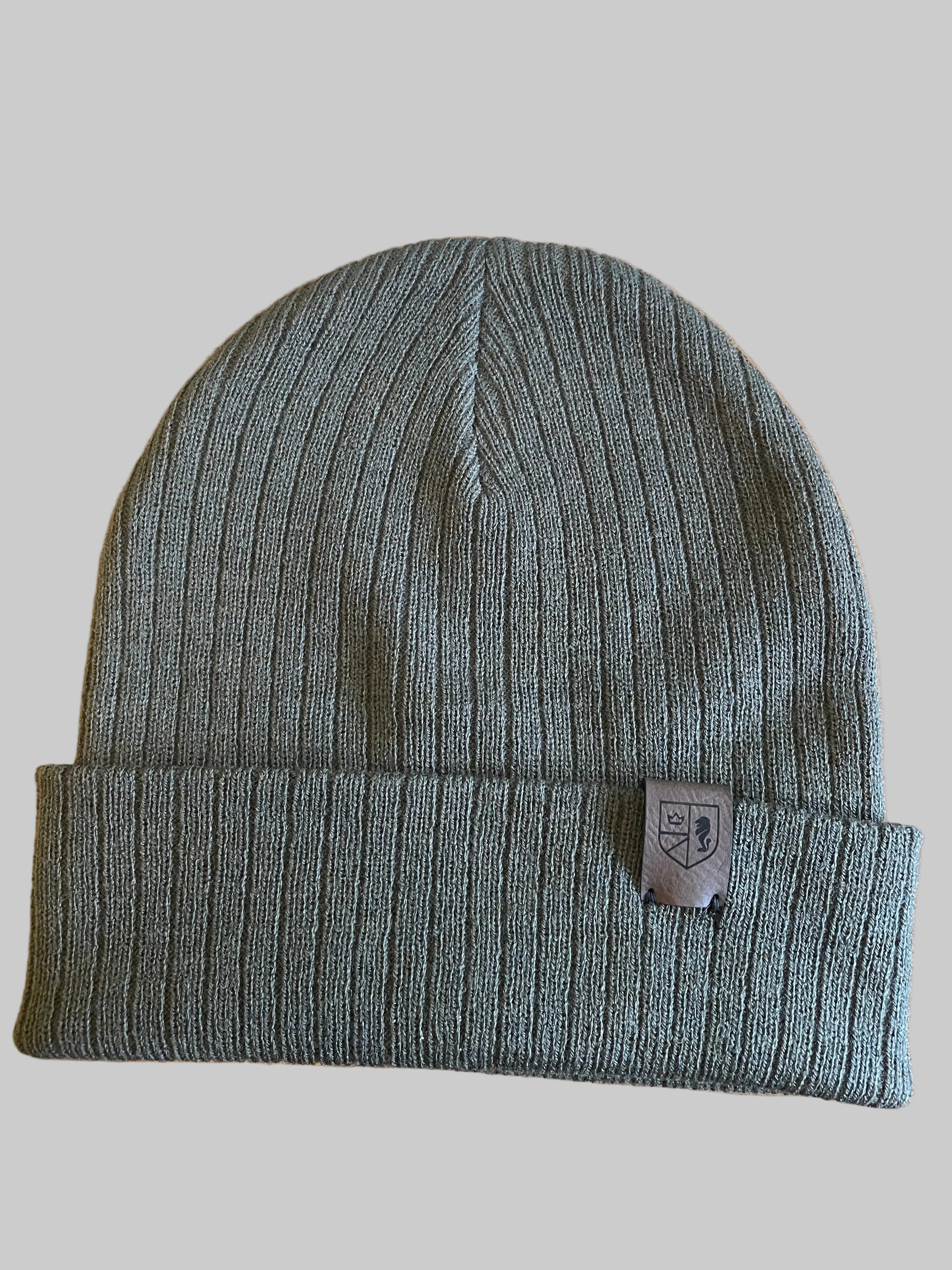 Olive Green knit beanie with a brand tag on a wooden surface next to a keyboard
